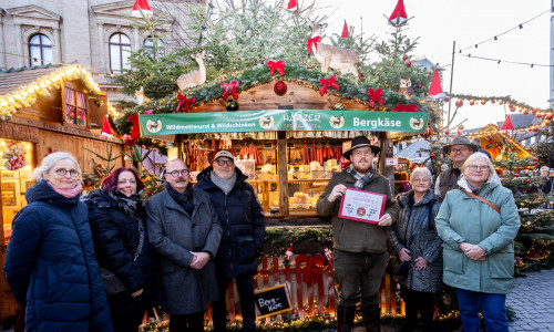 Der schönste Stand auf dem Braunschweiger Weihnachtsmarkt 2025 steht fest: „Harzer Spezialitäten“ bekommt in diesem Jahr die Auszeichnung überreicht: (v. l. n. r.) Cornelia Götz, Carolin Illmer, Karsten Ziaja, Olaf Jaeschke, Standbetreiber Franko Almstadt, Ulrike Neumann, Thomas Bronswyk und Bezirksbürgermeisterin Jutta Plinke.