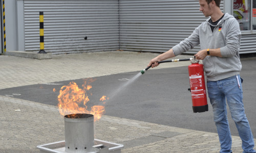 Ein Teilnehmer trainiert den sicheren Umgang mit dem Feuerlöscher an einem simulierten Brand.