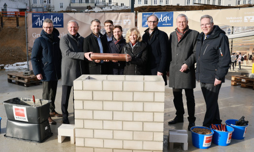 Grundsteinlegung am 15. Januar 2026 mit Zeitkapsel: André Triphaus-Woltermann (Geschäftsführer und technischer Vorstand der Köster Holding SE), Jürgen Brinkmann (Vorstandsvorsitzender der Volksbank BRAWO), Dennis Weilmann (Oberbürgermeister), Benjamin Maspohl (Projektentwickler der BRAWO RE Development Braunschweig), Sebastian Geese (Bereichsleiter Hochbau Braunschweig der Köster GmbH), Claudia Kayser (Leiterin der Direktion Wolfsburg der Volksbank BRAWO), Jens Hofschröer (Stadtrat und Dezernent für Digitales und Wirtschaft), Kai-Uwe Hirschheide (Erster Stadtrat und Stadtbaurat) und Ulf Müller (Geschäftsführer BRAWO RE Building Solutions). In der Zeitkapsel befindet sich eine Tageszeitung, Baupläne der BRAWO Arkaden, Polaroidfotos vom Eventtag sowie Impressionen und ein Poetry-Slam-Text vom 100-jährigen Jubiläum der Volksbank in Wolfsburg vom 6. November 2025.