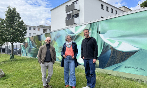 v. l. Künstler Sebastian Roese, Initiatorin und Antragstellerin Madeleine Stellmacher sowie Florian Martin (Citymanager der WMG) vor dem neuen Wandbild "Garten 35A" in der Kolpingstraße.