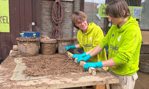Die Teilnehmer stellen Lehmwickel her, die als Füllmaterial zwischen Holzbalken dienen. 