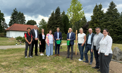 Mit einer symbolischen Baumpflanzung wurde die Übernahme des Friedhofsbetriebs in Neindorf durch die Stadt Wolfsburg zum 1. Juni 2026 sichtbar gemacht. Rund um den neu gepflanzten Baum versammelten sich Vertreterinnen und Vertreter aus Ortsrat, Stadtverwaltung und Kirche. Zu sehen sind unter anderem Oberbürgermeister Dennis Weilmann (Fünfter von links) und Superintendent Christian Berndt (Sechster von links).