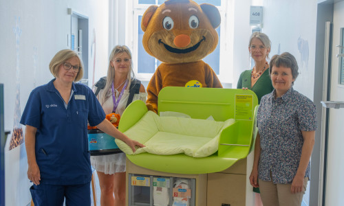 Das dm-Team um das Maskottchen SauBär übergab dem Team der Kinderchirurgie und -urologie des skbs sowie Chefärztin Dr. Andrea Schmedding (rechts) eine mobile Wickelstation.