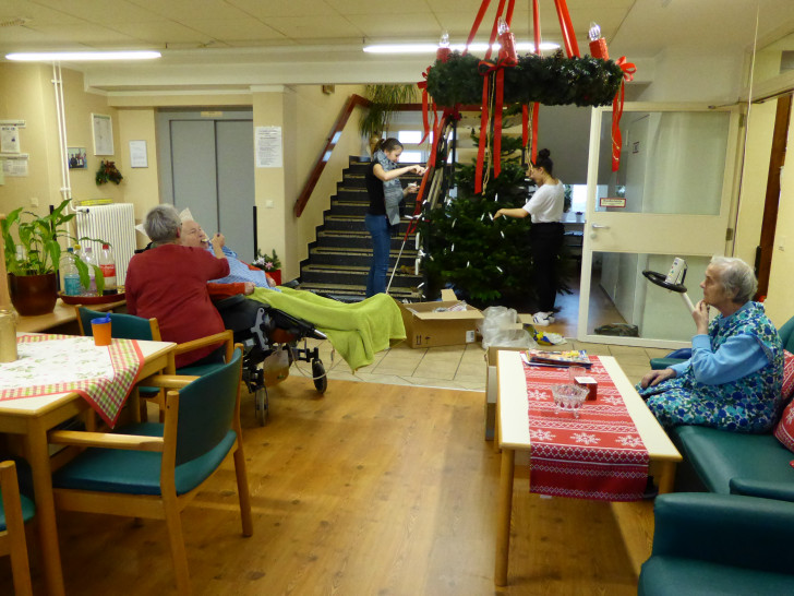 Sally und Hannah schmücken den Baum des Wohnbereiches Langhaus und die Bewohnerinnen nehmen aus etwas Entfernung daran Anteil, um die Verteilung der Lichterketten verbal zum begleiten. Foto: Privat