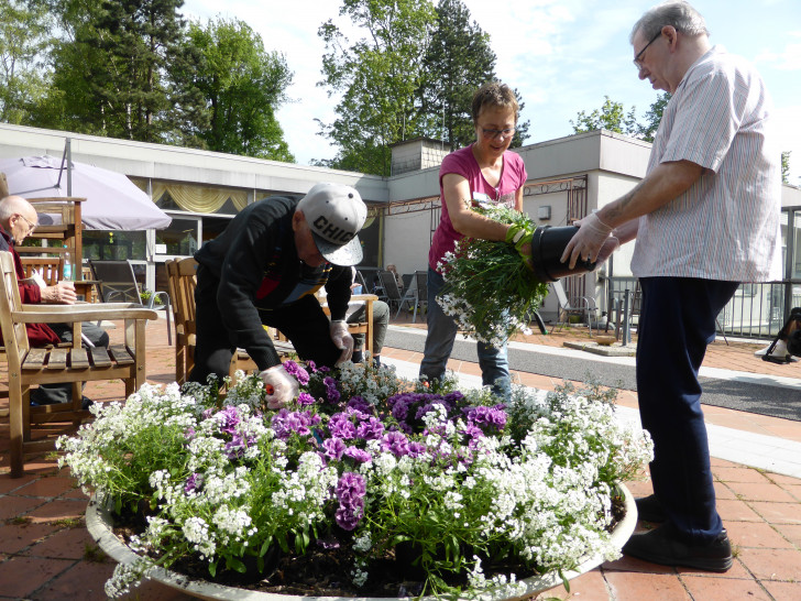 Bewohner der gerontopsychiatrischen Fachabteilung, die mit der Mitarbeiterin Ingrid Müsker eine große Blumenschale auf der Brücke bepflanzen. Foto: Seniorenbetreuung Schloß Schliestedt