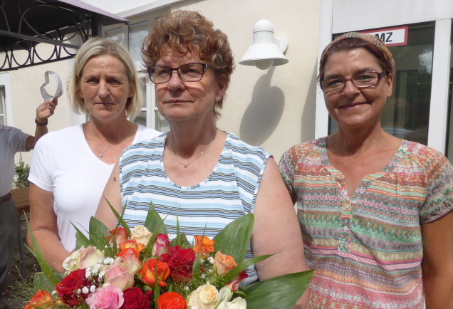 Die Dienstjubilarin Carola Ühre (Mitte) mit Blumenpräsent und zwei ihrer Kolleginnen vorm „Langhaus“ der Seniorenbetreuung Schloß Schliestedt. Foto: Seniorenbetreuung Schloß Schliestedt