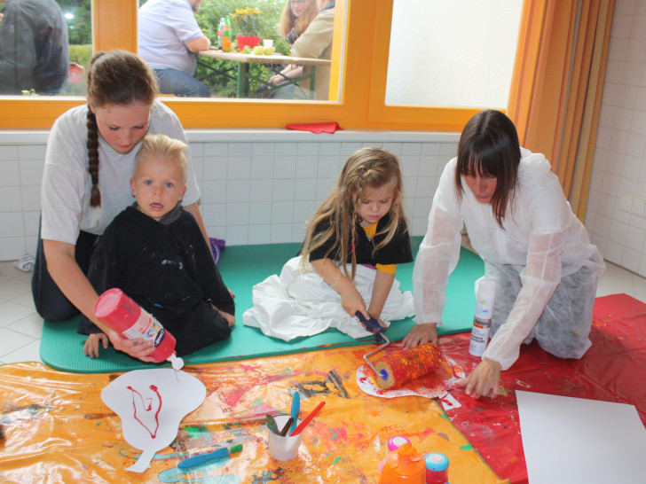 Im Matschraum des Kindergartens durften die Kinder nach Lust und Laune
mit Farben hantieren. Hier bemalen die Erzieherinnen Annika Bosse
(links) und Kerstin Drygall mit Tjard (zweiter von links) und Tanee aus
Papier ausgeschnittene Äpfel. Foto: Privat