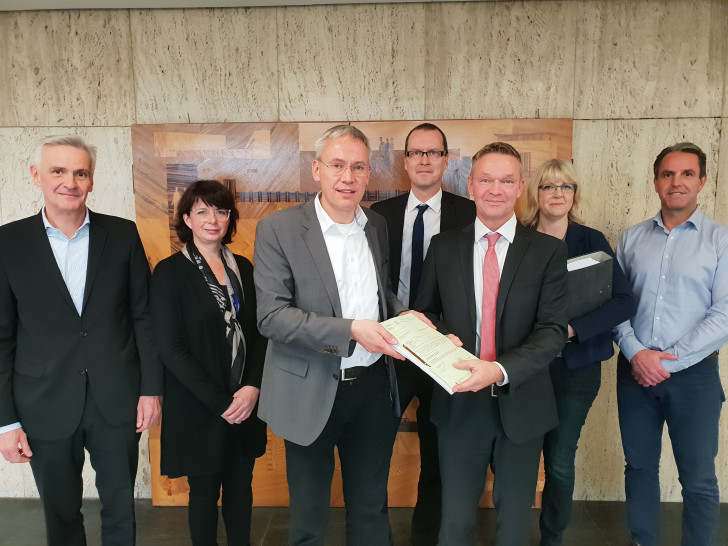 Stadtbaurat Kai-Uwe Hirschheide (dritter von links) übergibt die Baugenehmigung an Marco Meyer (Buhlmann Immobilien, dritter von rechts). Foto: Stadt Wolfsburg.