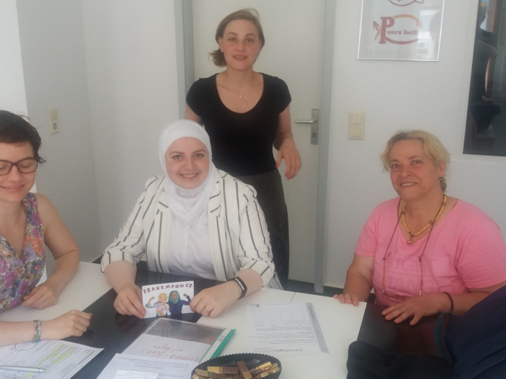 Hibatuallah Alzeer (Mitte sitzend) hilft ehrenamtlich Roveida Khomsi (rechts) im Alltag und bei der deutschen Sprache. Steffi Elena Bischoff (sehend) und Madeleine Martin (links) als Projektverantwortliche des Projektes „Frauenpower“ unterstützen dabei. Foto: Freiwilligenagentur Jugend-Soziales-Sport e.V. 