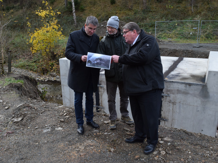 Wolfgang Lebzien (Mitte) zeigt Renke Droste (rechts) und Dr. Oliver Junk vor der neuen Brücke Fotos von den zerstörten Wegen in der Forst. Foto: Stadt Goslar