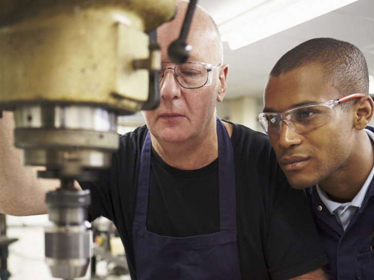 Ingenieur lehrt Azubi am Einsatz einer Fräsmaschine. Foto: Bundesagentur für Arbeit