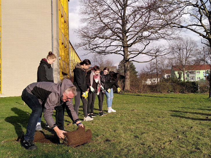 Stadtgärtnermeister Dirk Fellenberg führt den Schülern vor, wie der Rasen fachgerecht verlegt wird.