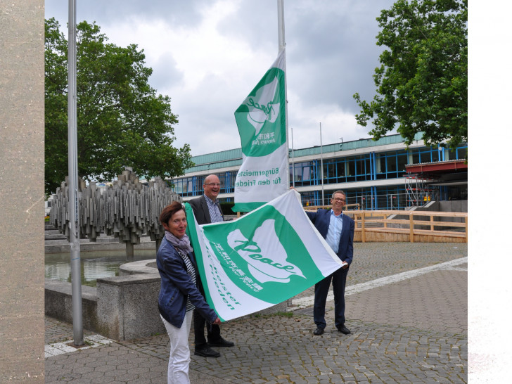 Klaus Mohrs, Bärbel Weist und Ingolf Viereck mit der "Mayors for Peace"-Flagge vor dem Wolfsburger Rathaus.