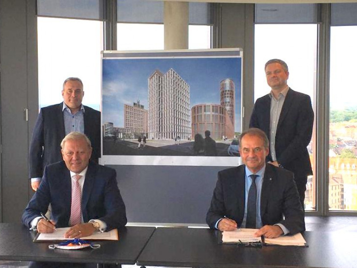 Jürgen Brinkmann (vorne links) und Ulrich Markurth (vorne rechts) bei der Vertragsunterzeichnung. Im Hintergrund sind Klaus Gattermann (links) und Carsten Beddig (rechts) zu sehen. Zwischen ihnen ist das geplante Gebäude zu erkennen.