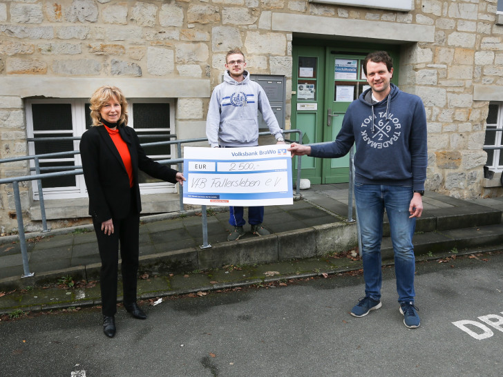 Claudia Kayser, Leiterin der Direktion Wolfsburg der Volksbank BraWo, übergibt den symbolischen Spendenscheck an Dr. Nicolas Heidtke (r.), 1. Vorsitzender des VfB Fallersleben, und Tom-Lukas Behrens (Mitte), Spieler der 2. Herren Fußball.   