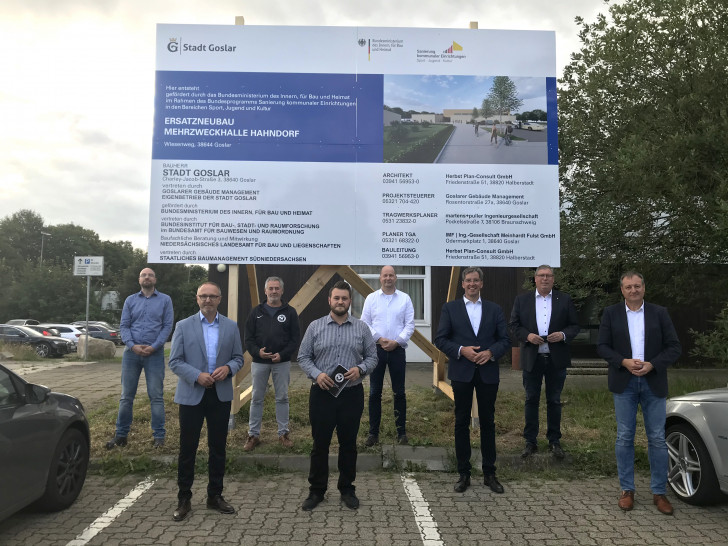 Tobias Brandt (Goslarer Gebäudemanagement GGM), Norbert Schecke (Ratsherr CDU), Joachim Bürdeck (Geschäftsführer SV Hahndorf), Pascal Czwojdrak (Vorsitzender SV Hahndorf), Rüdiger Heine (Vorsitzender RC Germania Hahndorf), Oberbürgermeister Dr. Oliver Junk, Erster Stadtrat Burkhard Siebert und Oliver Heinrich (Betriebsleiter GGM) unter dem neuen Bauschild, das den Beginn der Neubaumaßnahme markiert (v. li.).