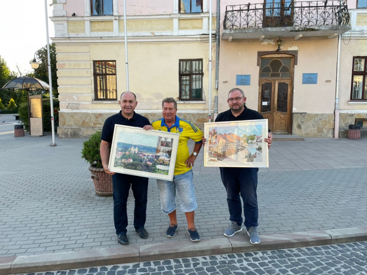 Besuch des 5. Hilfstransportes (August 2022) in Solotschiw gefahren sind. Peter Voß (Vorsitzender PVS, Mitte) und Jan Fricke (Vereinsmitgleid und stellv. Landrat) übergeben Bilder aus und von der Partnerstadt Schöningen an Solotschiws Bürgermeister Íhor Grynkiv vor dem Rathaus in Solotschiw.