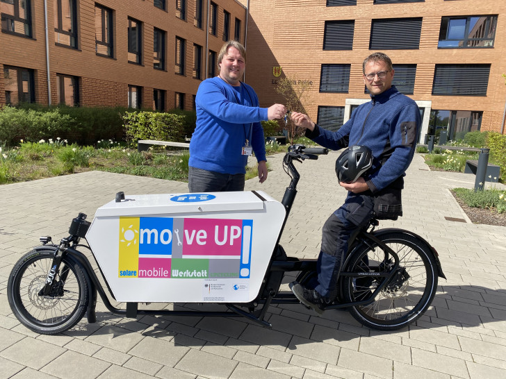 Hausmeister Andreas Jensch (rechts) übernimmt die Lastenradschlüssel vom Initiator des Projektes moveUP Martin Schlüter von der Klimaschutzagentur.