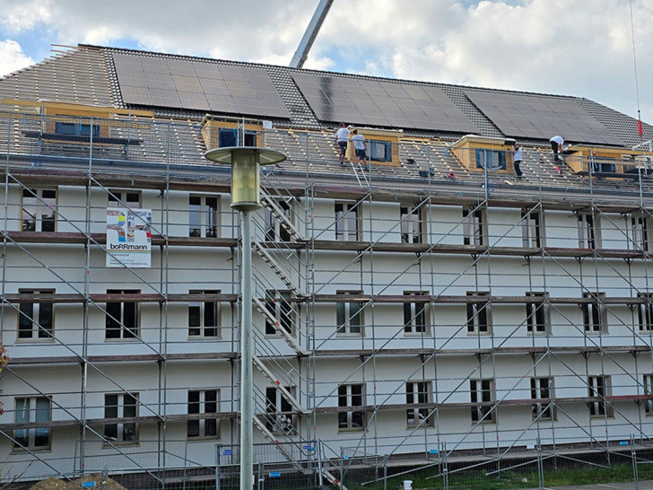 Das Gebäude erhält eine Photovoltaikanlage: Monteure arbeiten an der Installation der Module auf dem Dach.