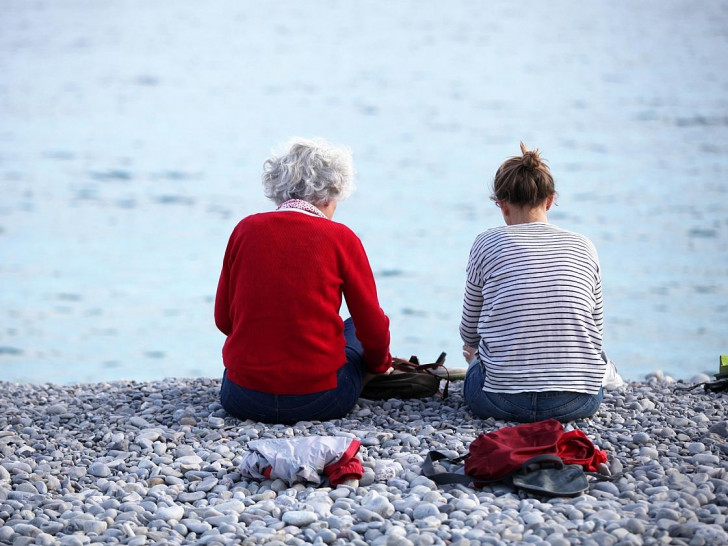 Alte und junge Frau sitzen am Strand