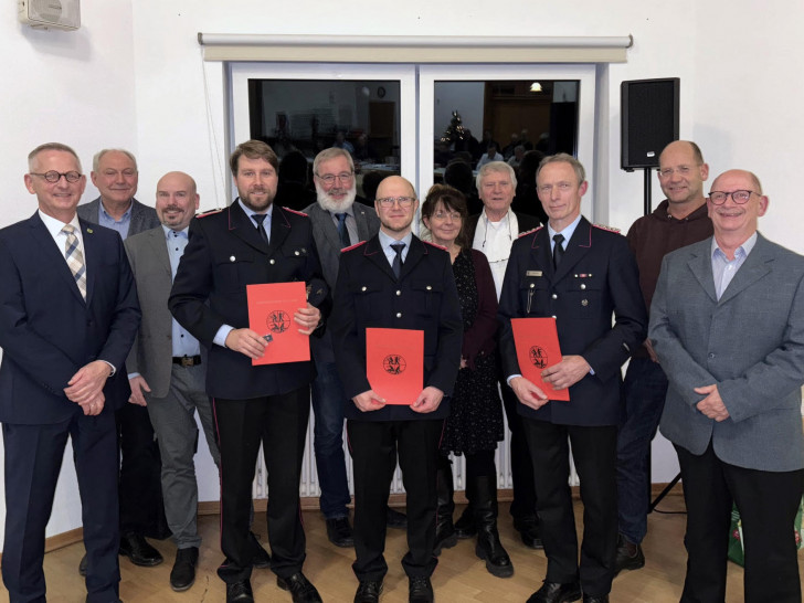 Dirk Neumann, ganz links, mit den Feuerwehrmännern (v. l.) Kevin Müller, Alexander Jacob und Peter Thiele, eingerahmt von Rats- und Verwaltungsmitgliedern.