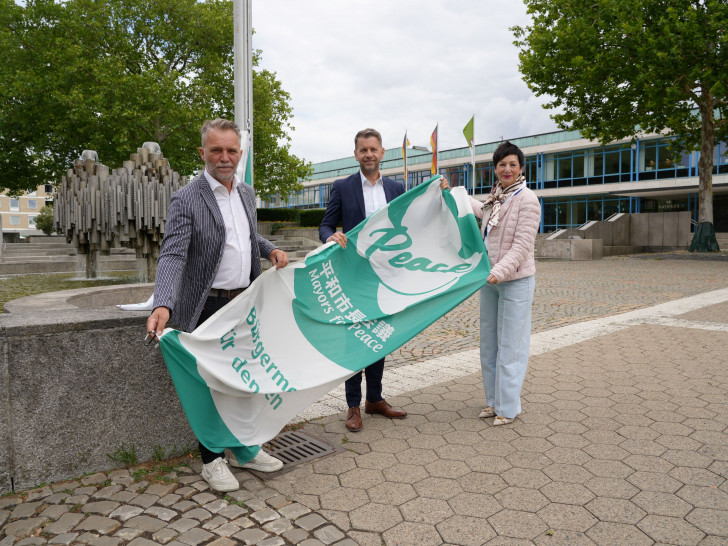Oberbürgermeister Dennis Weilmann (Mitte) hisst gemeinsam mit Andreas Klaffehn und Immacolata Glosemeyer die Mayors for Peace-Flagge. 