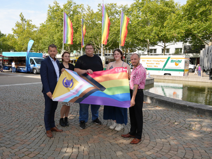 Oberbürgermeister Dennis Weilmann und Britta Deike (Gleichstellungsreferat Stadt Wolfsburg) präsentieren gemeinsam mit den Organisatoren des CSD Wolfsburg - Luke Bärthel, Isabell Kleindienst und Kevin Kluge - die offizielle Flagge (v. li.).