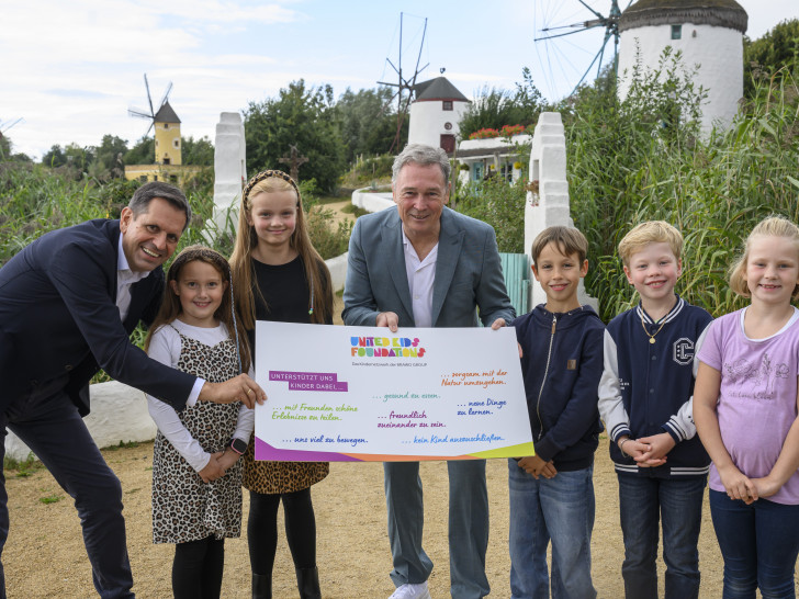Der niedersächsische Ministerpräsident Olaf Lies (links) wird gemeinsam von Thomas Fast, Vorstandsvorsitzender der Volksbank BRAWO Stiftung und langjähriger Botschafter von United Kids Foundations, und Kindern des Netzwerks im Gifhorner Mühlenmuseum als neuer Schirmherr begrüßt.
