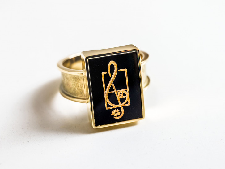 Die viereckige Fassung des Steins unterstreicht den klaren, modernen Charakter des Rings. Ein Notenschlüssel als Zeichen für musikalischen Ausdruck, ein Kleeblatt als Hinweis auf den Verleihungsort Hahnenklee sowie die Fibonacci-Spirale, die für Harmonie und das Streben nach Perfektion steht, ergänzen das gelungene Arrangement.