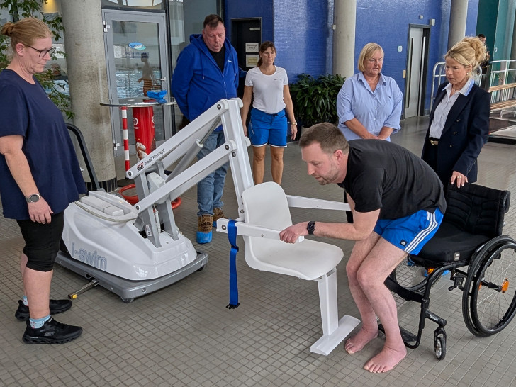 Premiere im Aquantic: Björn Lehrke-Ahrens nimmt im Beisein von Oberbürgermeisterin Urte Schwerdtner (v. re.), Andrea Simon, Behindertenbeauftragte der Stadt Goslar, und Meik Erbrecht (2. v. li.), Technischer Leiter des Bäderbetriebs, sowie zwei Schwimmmeisterinnen auf dem neuen Schwimmbadlifter Platz.