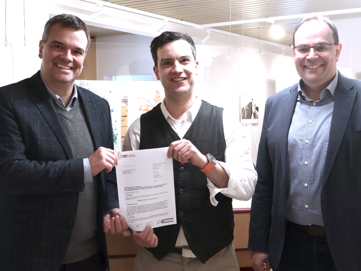 Landrat Dr. Alexander Saipa (links) überreicht im Beisein von Langelsheims Bürgermeister Ingo Henze (rechts) Dr. Alexandro Hoyer Sepulveda einen Förderbescheid über 50.000 Euro.  