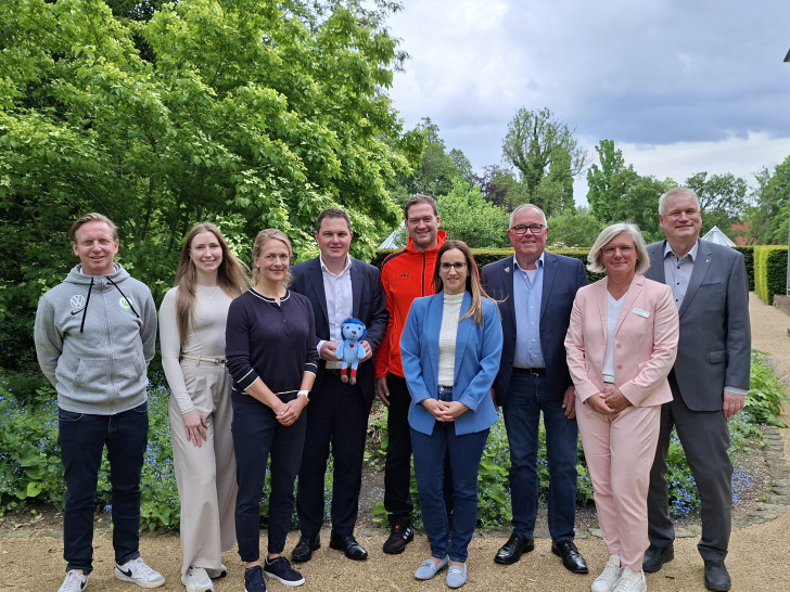 Bei der Vorstellung der Studienergebnisse (von links): Roy Präger vom VfL Wolfsburg, Marleen Stridde von der Audi BKK, Studienkoordinatorin Melanie Lemke vom Universitätsklinikum Hamburg-Eppendorf, Landrat Philipp Raulfs, Miroslav Jenka, Trainer bei den Grizzlys, Projektleiterin Janine Ahrends von der Gesundheitsförderung und Prävention des Landkreises Gifhorn, Norbert Blyszcz, Vorstandsmitglied der Young Grizzlys Wolfsburg, Nele Westphal, Fachbereichsleiterin Kinder, Jugend und Familie beim Kreisverband Gifhorn des Deutschen Roten Kreuzes, und Kreisrat und Gesundheitsdezernent Rolf Amelsberg. Landrat Philipp Raulfs hält das Maskottchen Tobi des Bewegungsprojekts in den Händen.