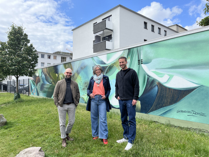 v. l. Künstler Sebastian Roese, Initiatorin und Antragstellerin Madeleine Stellmacher sowie Florian Martin (Citymanager der WMG) vor dem neuen Wandbild "Garten 35A" in der Kolpingstraße.