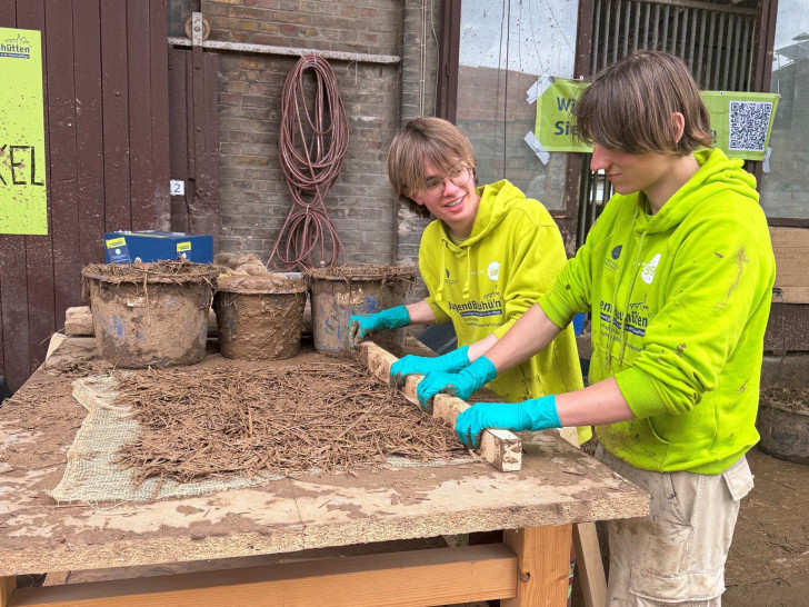 Die Teilnehmer stellen Lehmwickel her, die als Füllmaterial zwischen Holzbalken dienen. 