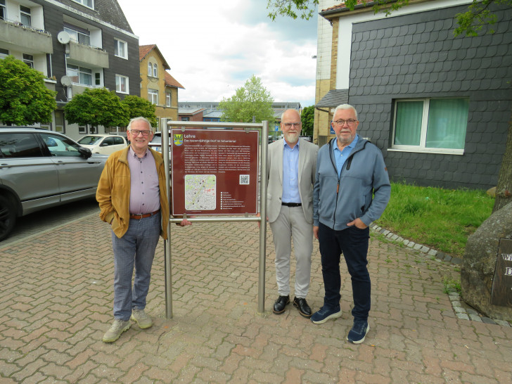 Ortsheimatpfleger Wilhelm Knigge, Verwaltungsleitung Tobias Breske und Ortsbürgermeister Heinrich Köther mit der neuen Infotafel auf dem Marktplatz.