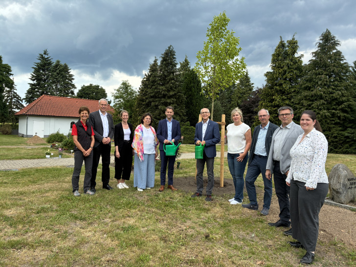 Mit einer symbolischen Baumpflanzung wurde die Übernahme des Friedhofsbetriebs in Neindorf durch die Stadt Wolfsburg zum 1. Juni 2026 sichtbar gemacht. Rund um den neu gepflanzten Baum versammelten sich Vertreterinnen und Vertreter aus Ortsrat, Stadtverwaltung und Kirche. Zu sehen sind unter anderem Oberbürgermeister Dennis Weilmann (Fünfter von links) und Superintendent Christian Berndt (Sechster von links).