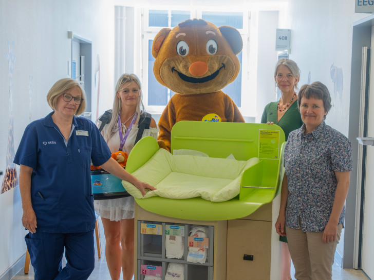 Das dm-Team um das Maskottchen SauBär übergab dem Team der Kinderchirurgie und -urologie des skbs sowie Chefärztin Dr. Andrea Schmedding (rechts) eine mobile Wickelstation.